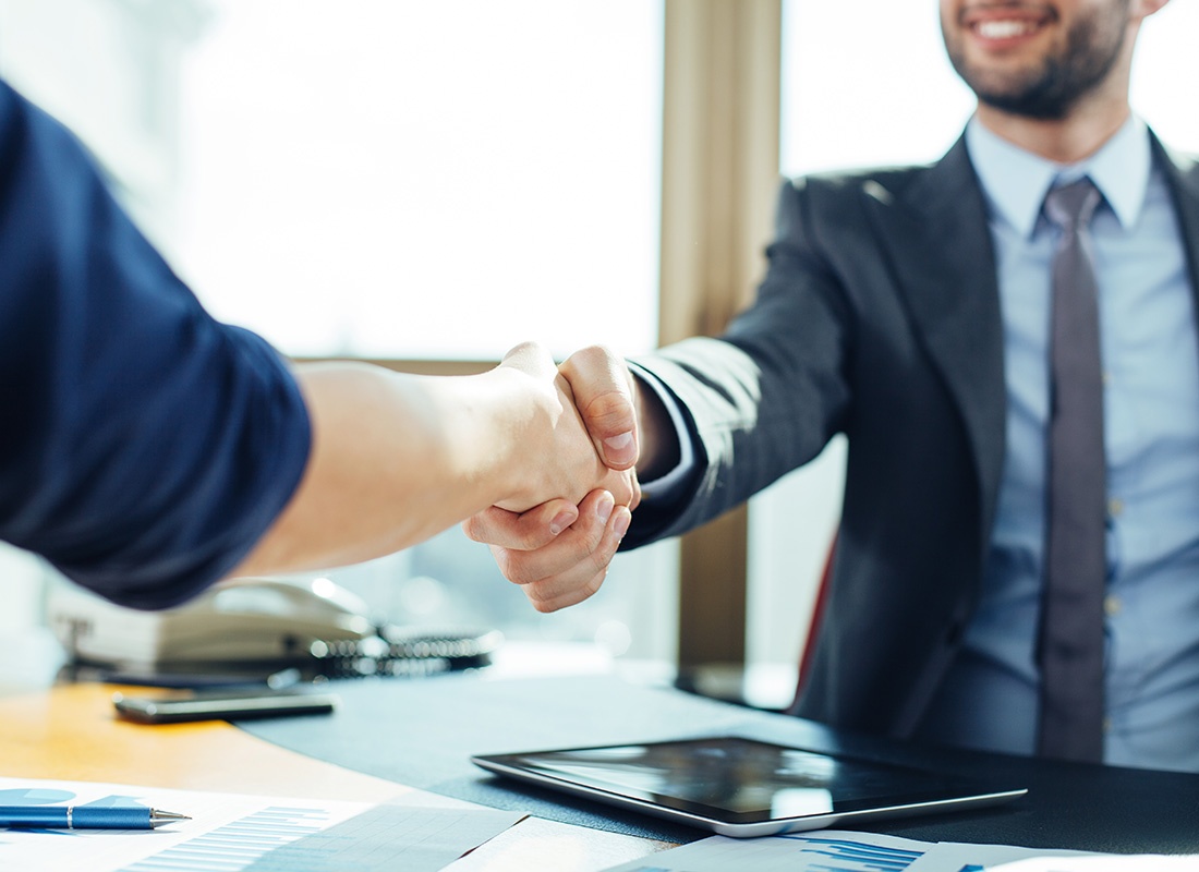 About Our Agency - Closeup View of Two Business People Shaking Hands Over a Desk in an Office During a Business Meeting