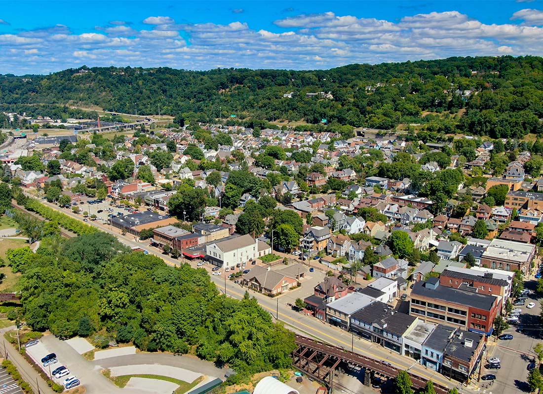 Bridgeville, PA - Aerial View of Commercial Buildings and Homes Surrounded by Green Trees and Mountains in Bridgeville Pennsylvania