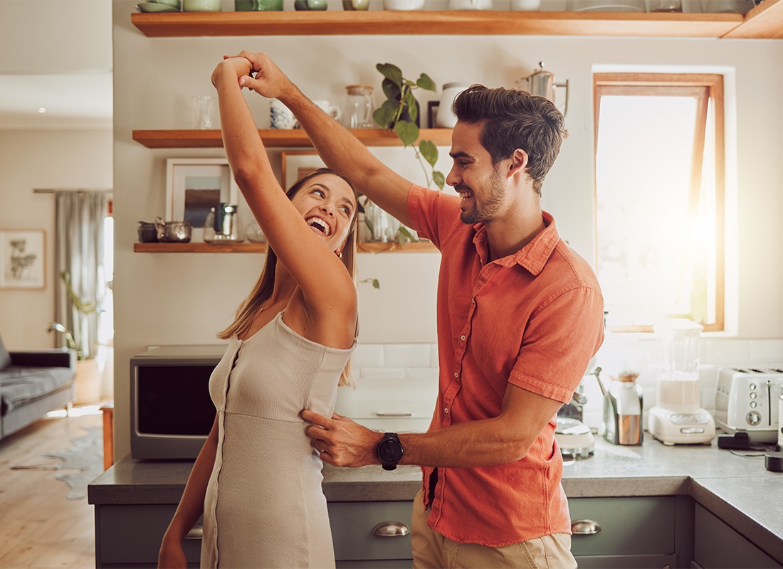 Personal Insurance - Portrait of a Cheerful Young Married Couple Having Fun Dancing in Their Bright Modern Kitchen