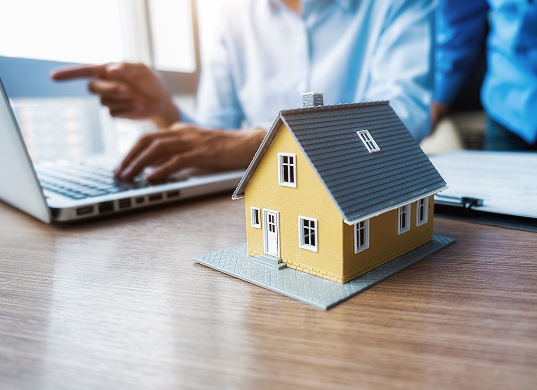 Association Certificate Request - View of a Model House Sitting on a Wooden Table Next to a Businessman Using a Laptop in an Office